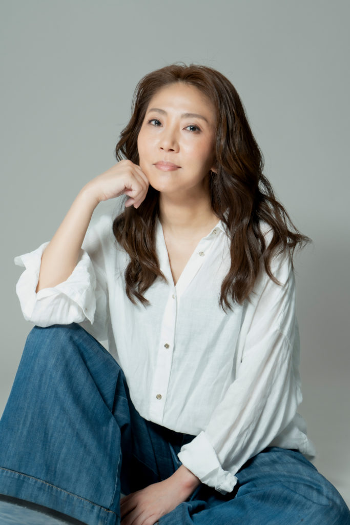 白いシャツを着た女性が顎に手を置き座っている