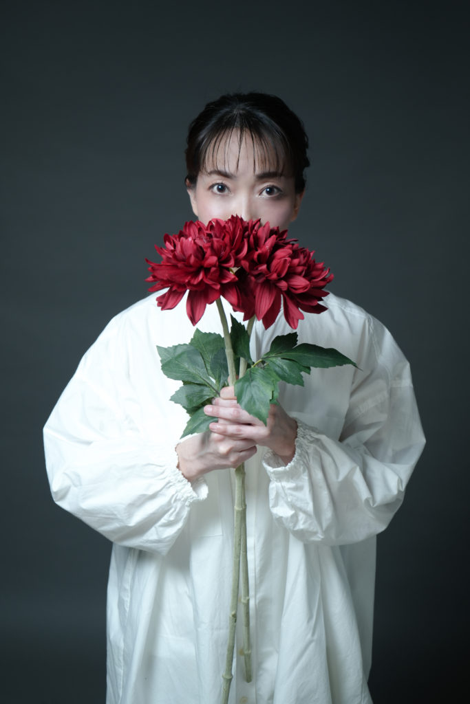 ダリアの花を持ち口元を隠した女性の写真