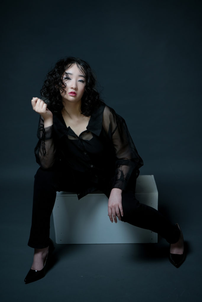 黒の服を着た女性が白色のボックスに座りポージングをしている写真