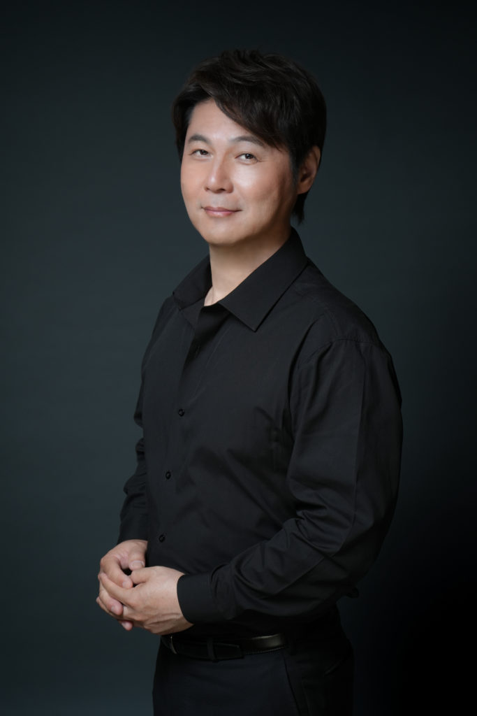 黒のシャツを着た男性がポーズをつけて笑顔の写真