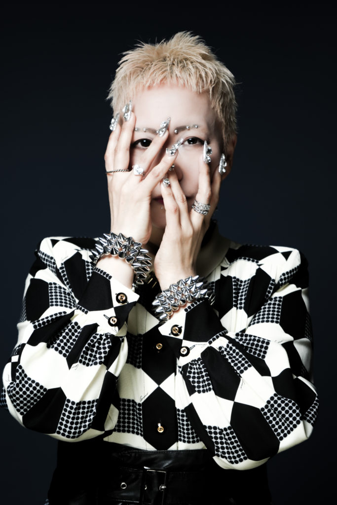 金髪で顔にピアスを付けた女性が手で顔を覆う写真